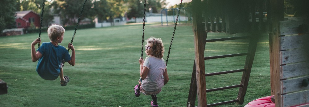 Zwei Kinder schaukeln auf einem Spielplatz